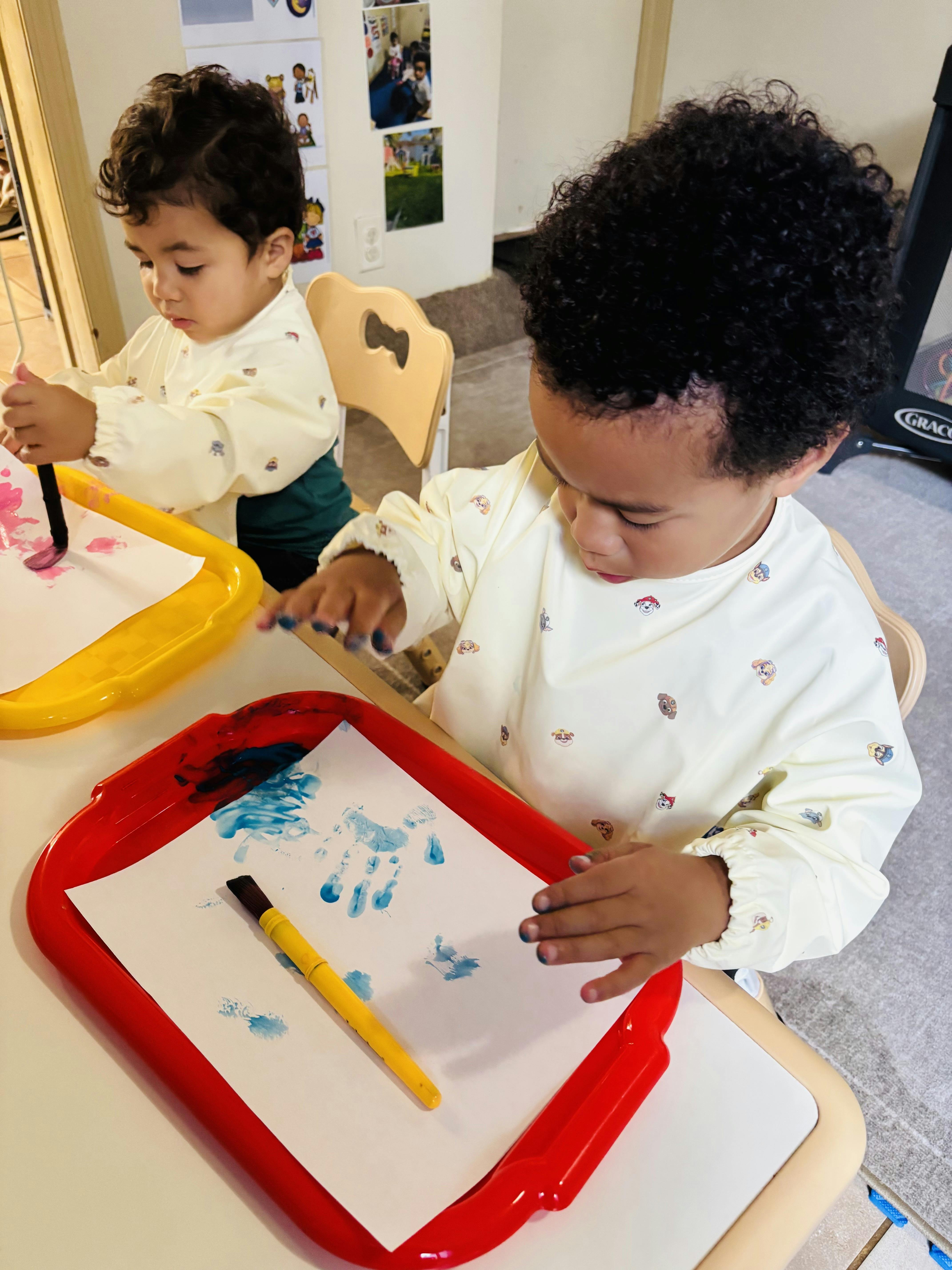 Two children painting on paper at tables in a classroom
