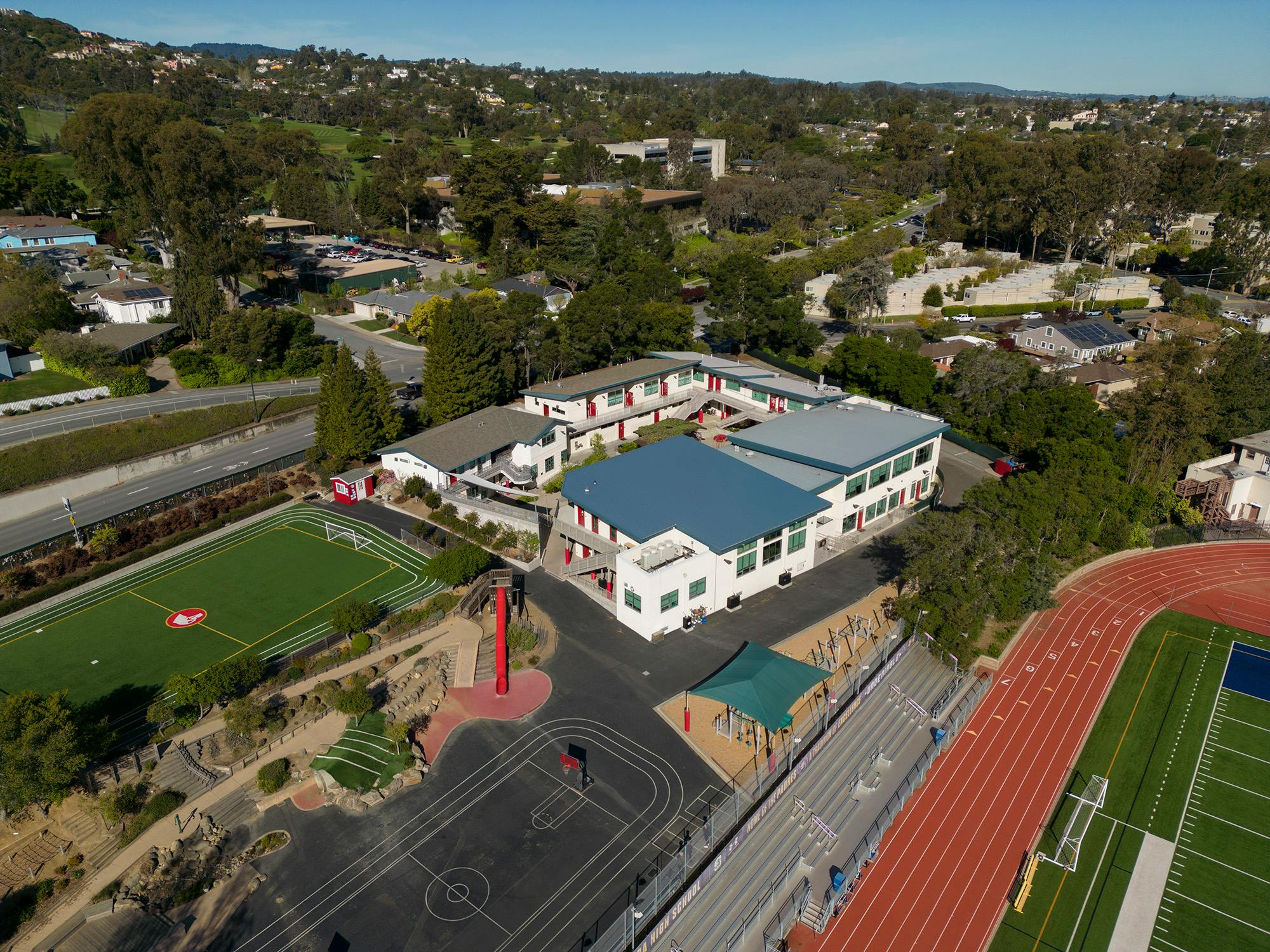Aerial view of a school building with a blue roof next to a sports field and track
