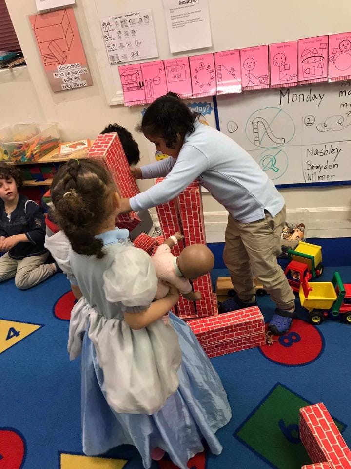 Two children playing with large red blocks, one holding a doll