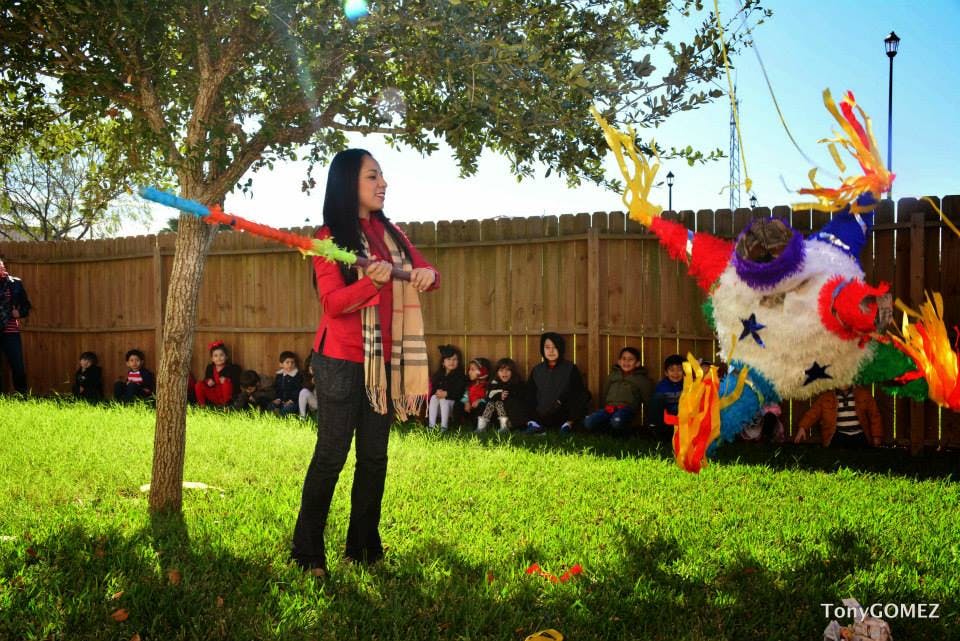 Person holding a stick, about to hit a piñata, with children watching
