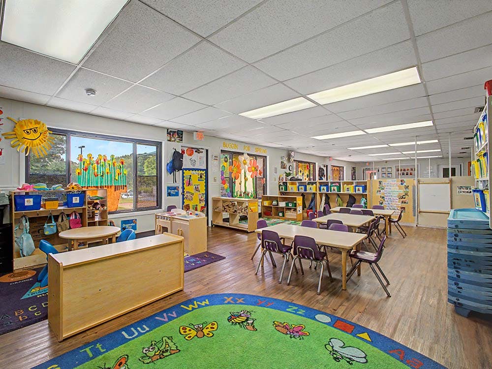 Colorful classroom with small tables and chairs, a large alphabet rug, and bright decorations