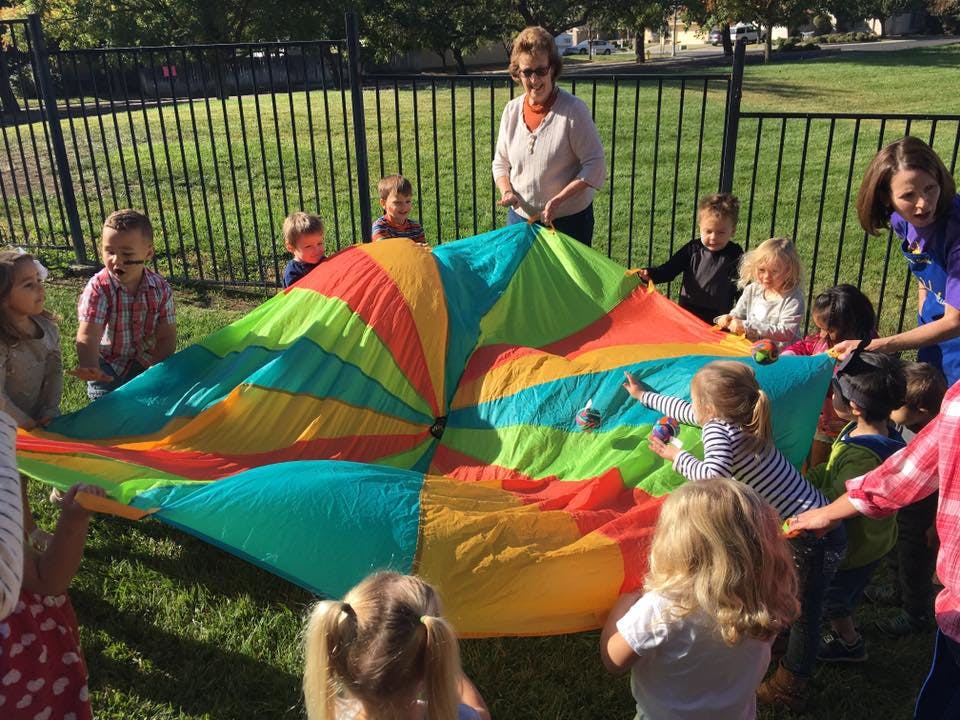 Adults and children playing with a colorful parachute outdoors