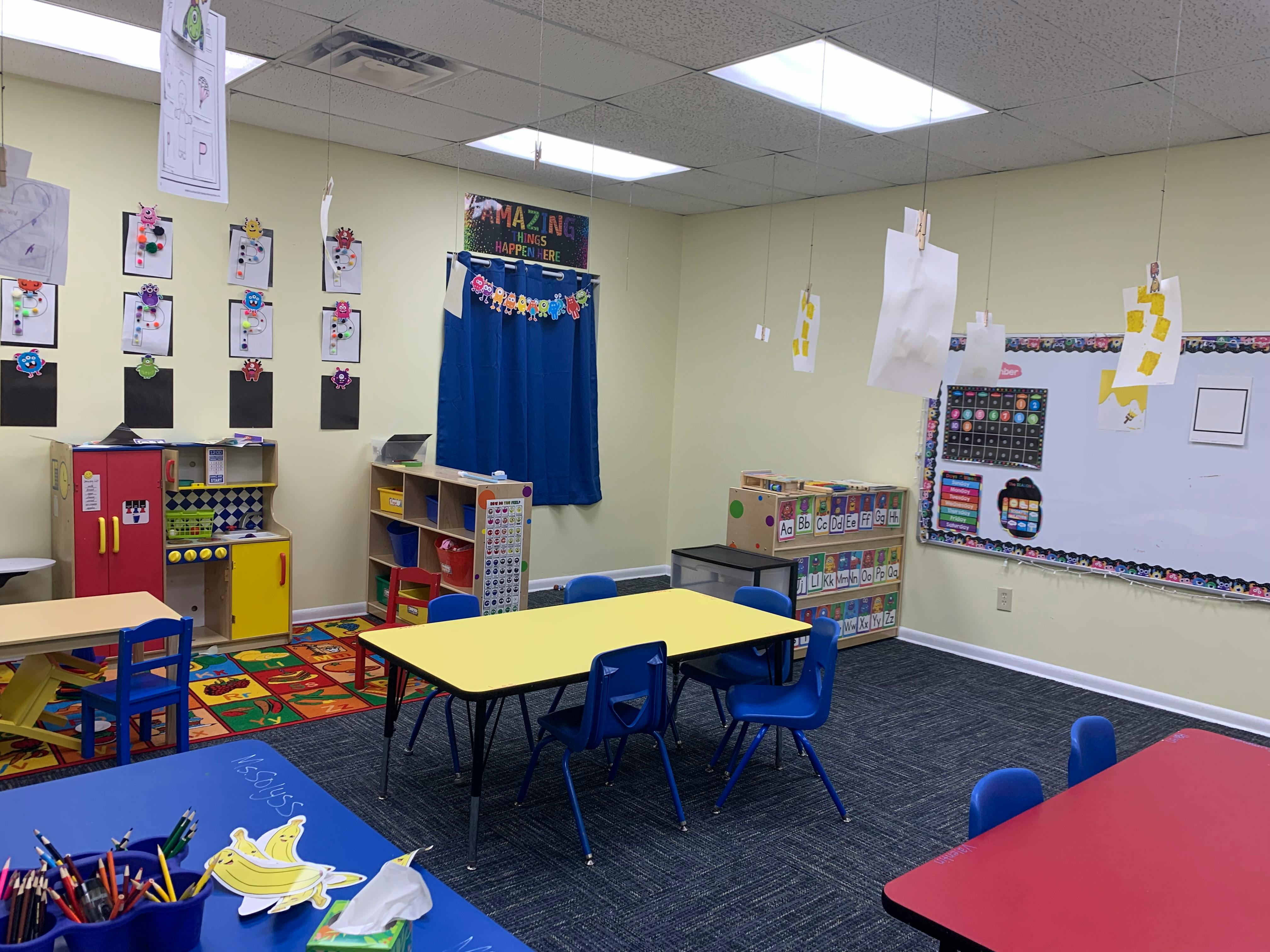 Empty classroom with colorful tables and chairs, and children's artwork on walls