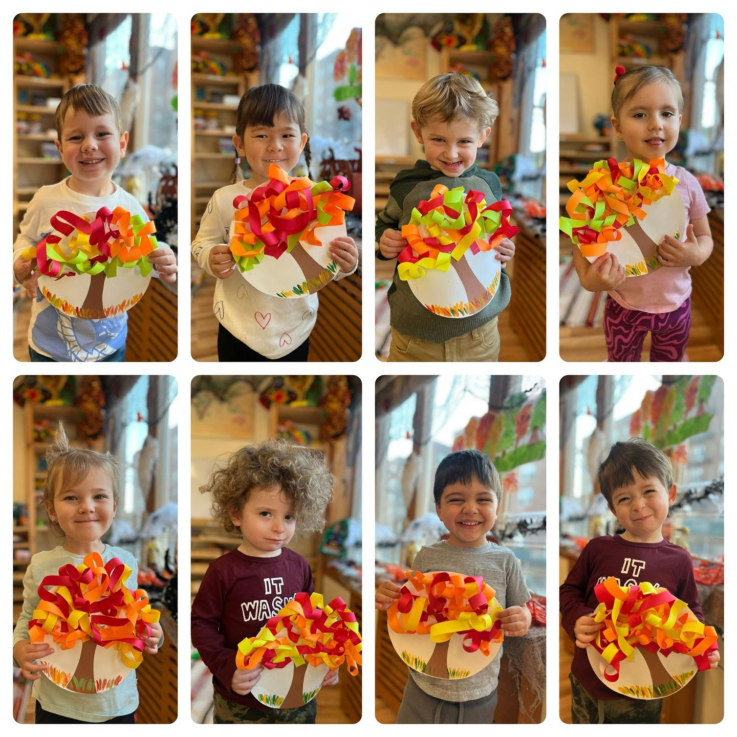 Eight children holding up paper tree crafts with colorful leaves