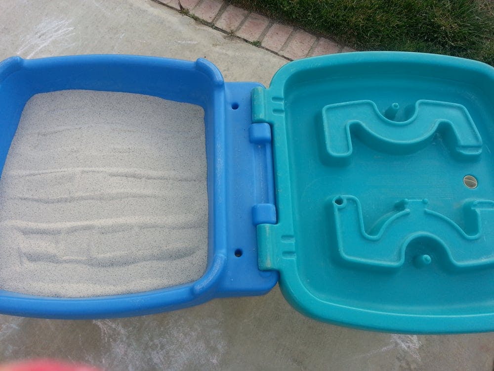 Blue plastic sandbox with sand and a lid with a molded track