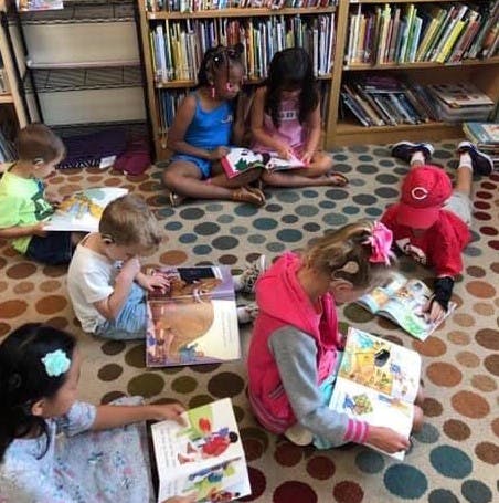 Children sitting on a patterned rug reading books in a library