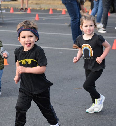 Two children running on pavement with orange cones in the background