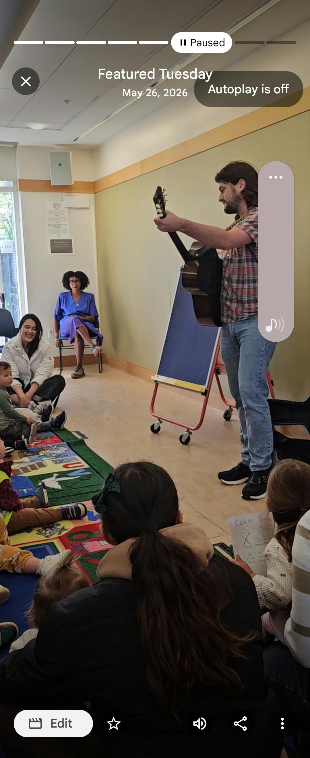 A person playing acoustic guitar for a group of children and adults