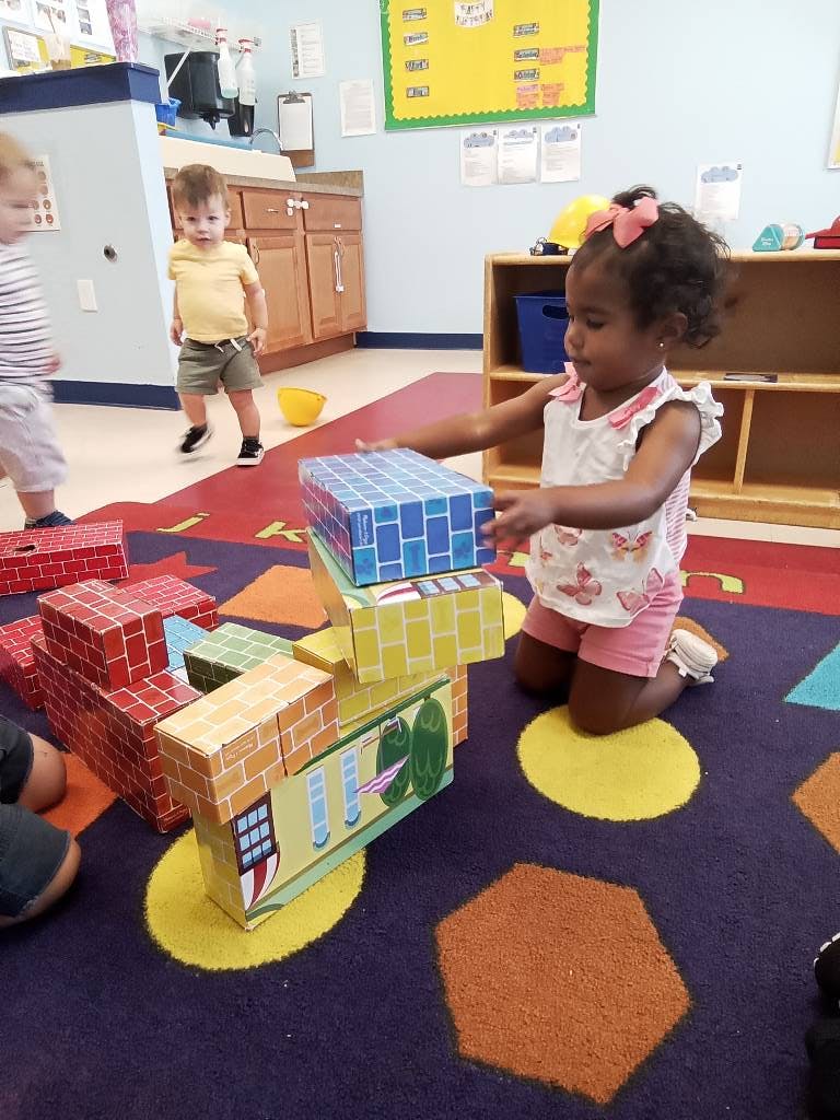 Child kneeling on a rug, stacking large blocks in a classroom