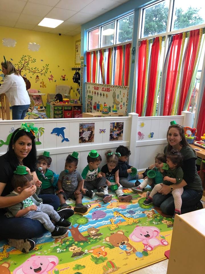 Adults and children sitting on a colorful mat in a classroom