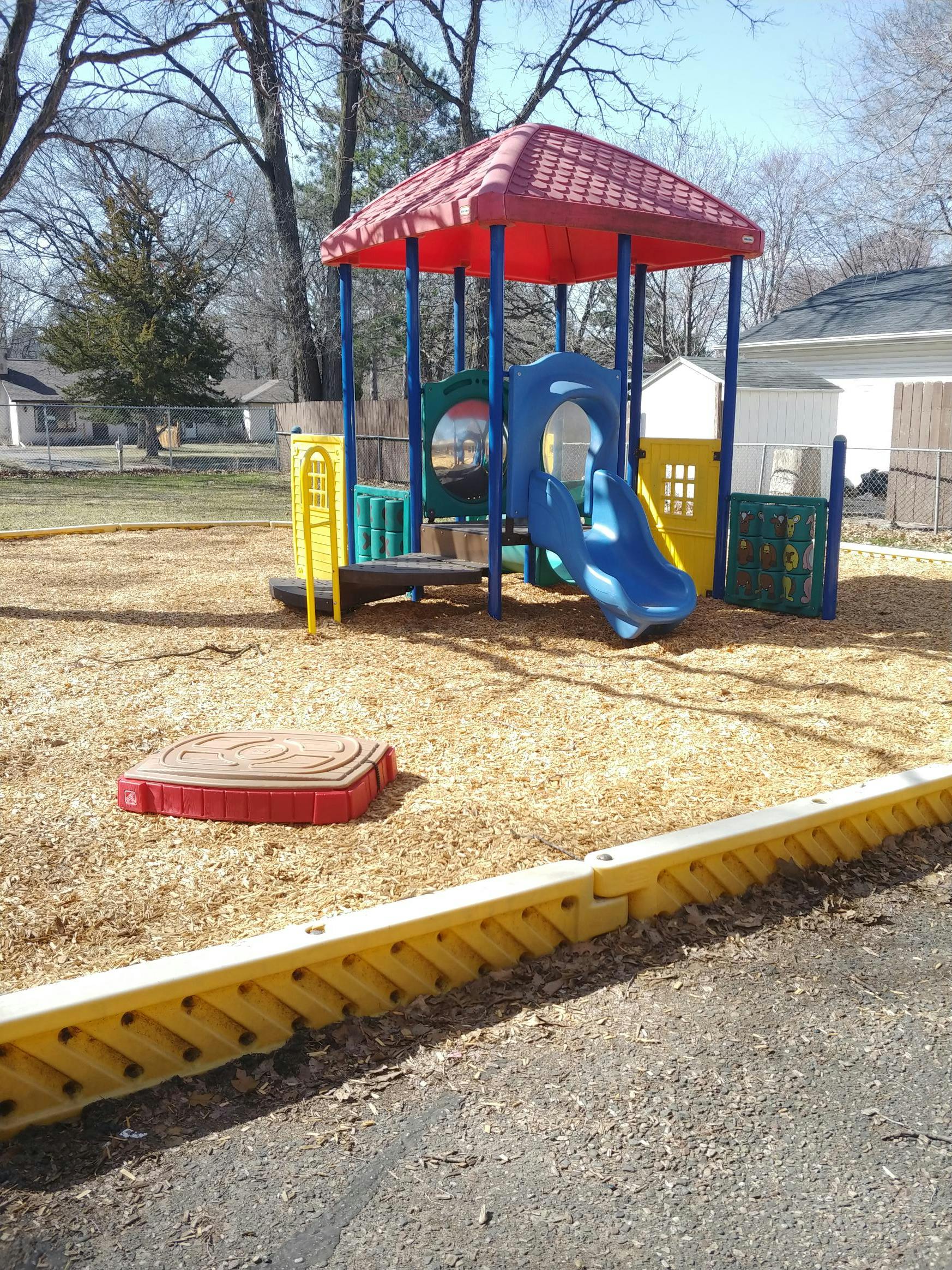 Playground with a red-roofed structure, blue slide, and wood chip ground