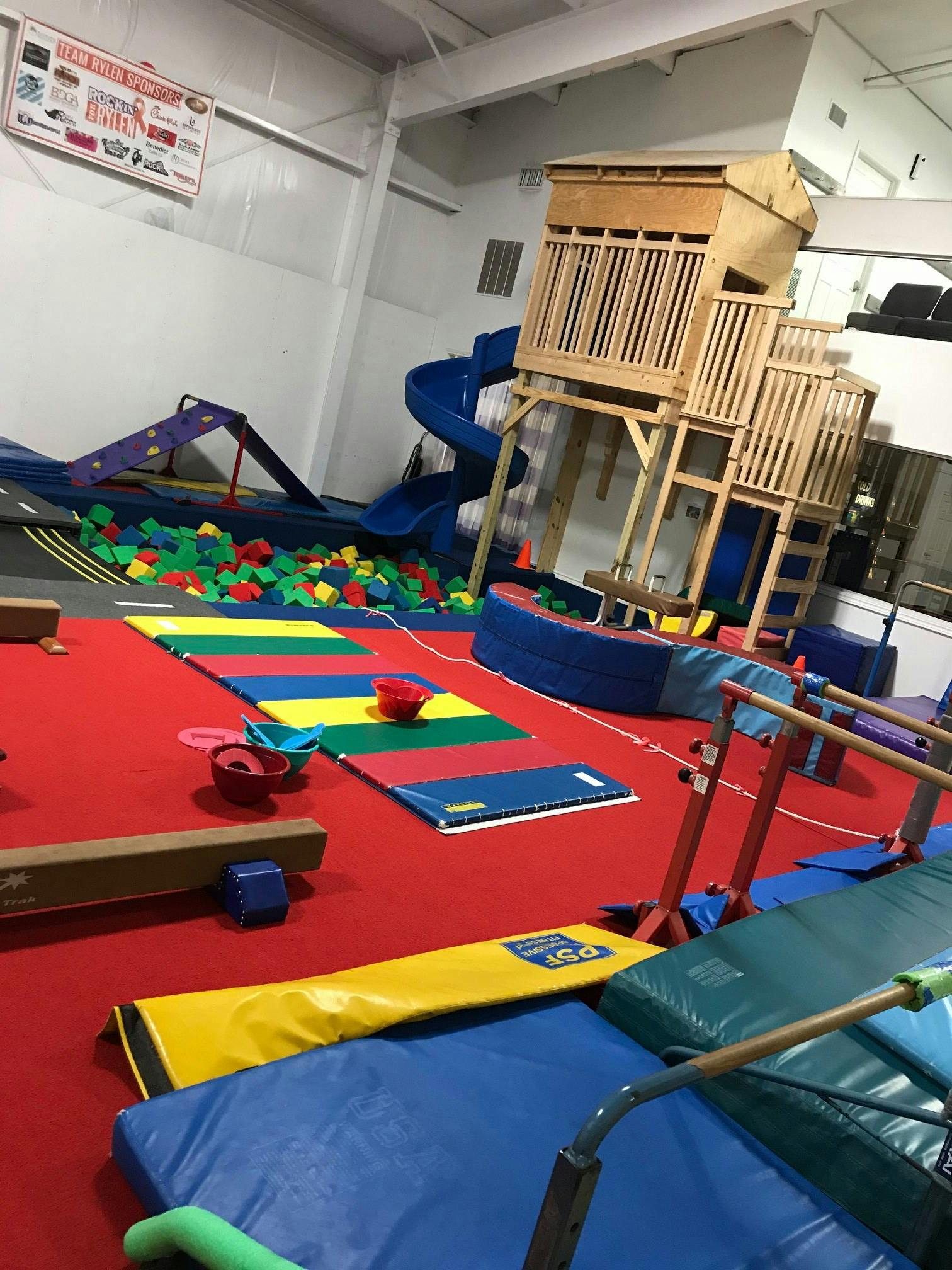 Indoor play area with a wooden play structure, blue slide, and ball pit