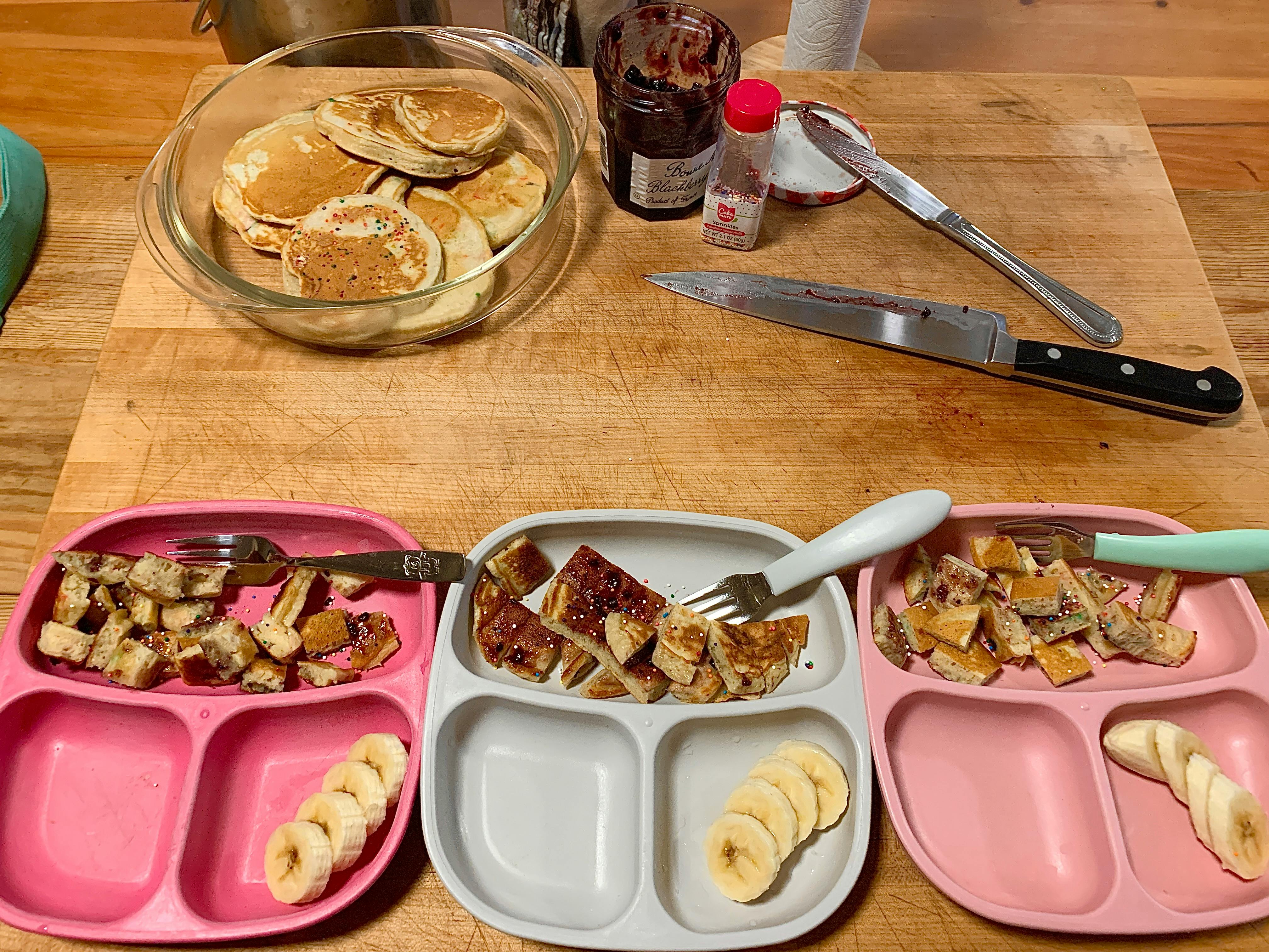 Pancakes in a glass bowl, with three plates of cut pancakes and bananas