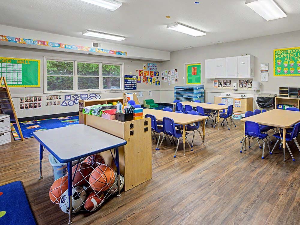 Classroom with tables, blue chairs, educational decorations, and a ball net under a desk
