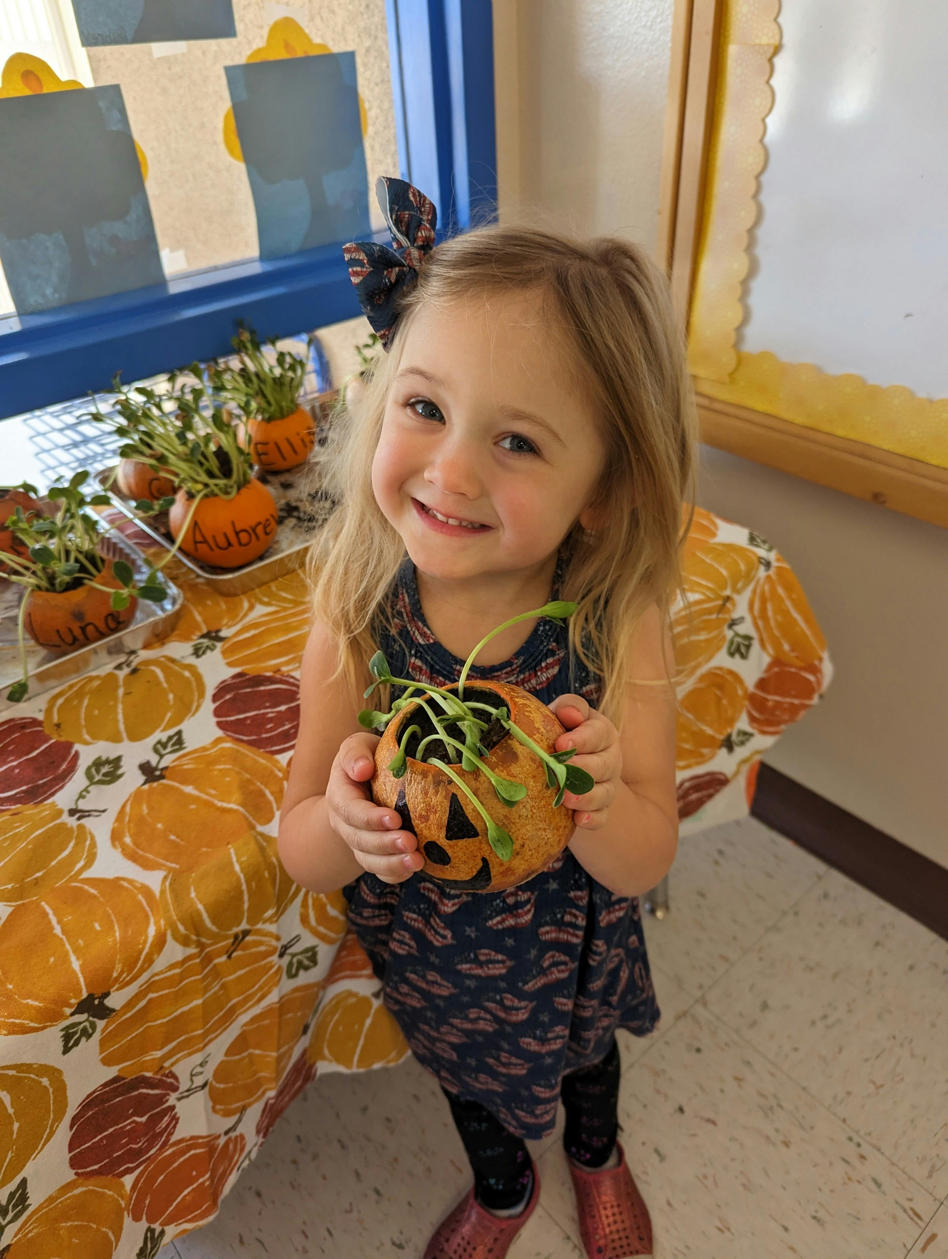Child holding a small pumpkin with sprouts growing from it