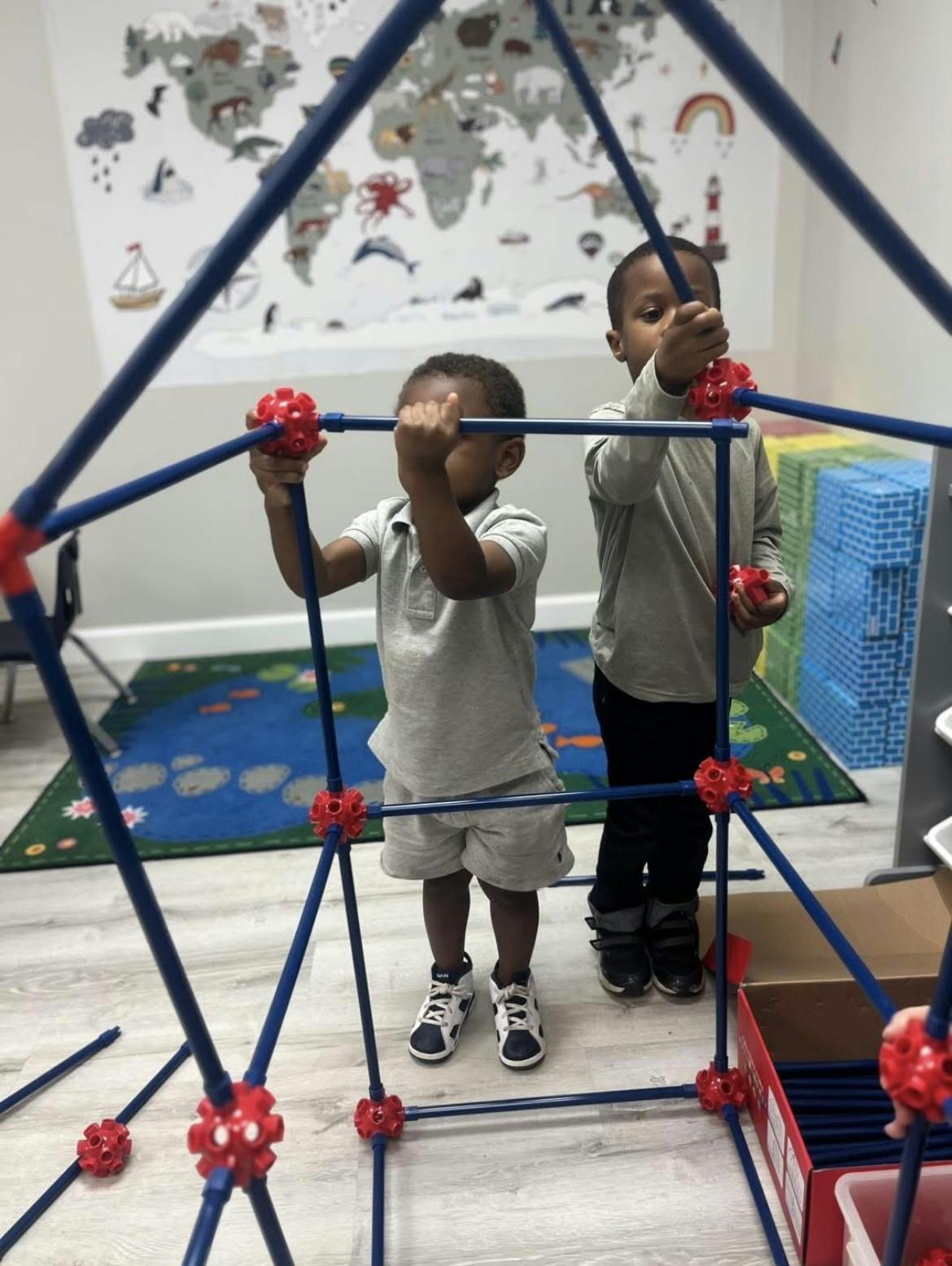 Two children building a structure with blue poles and red connectors