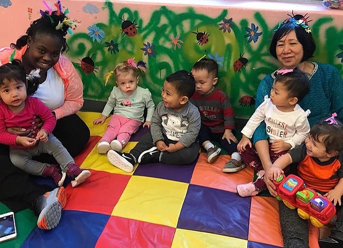 Two people sitting on a colorful mat with several children