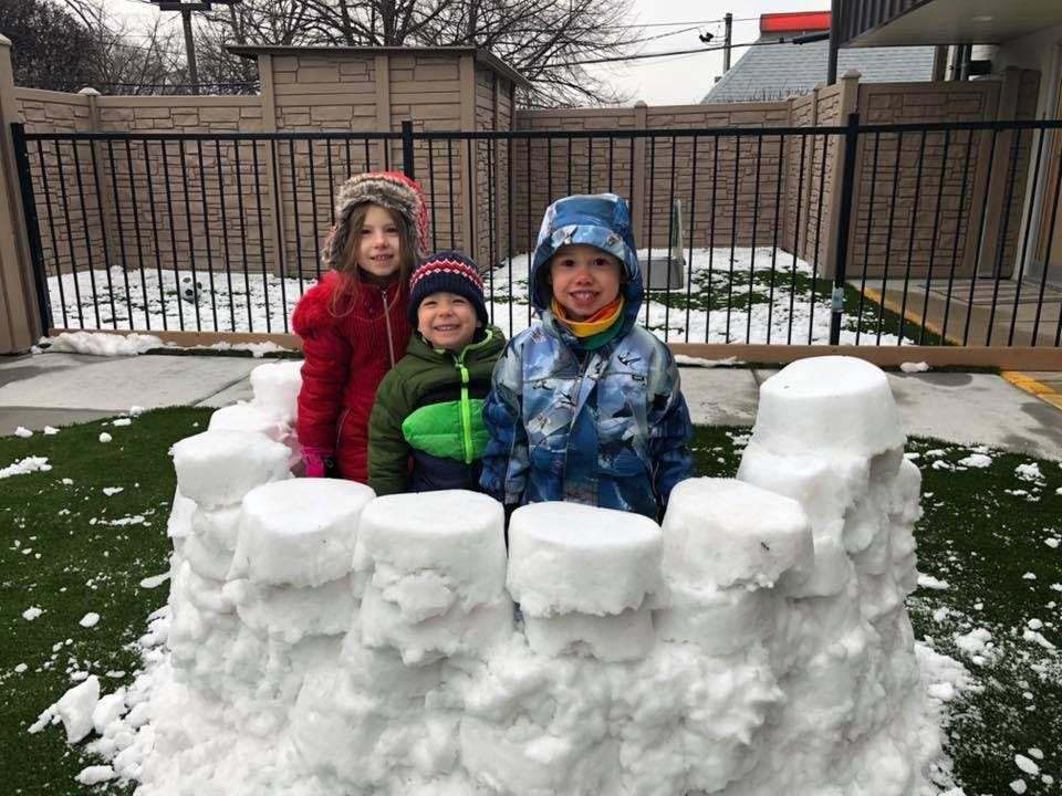 Three children standing behind a snow fort