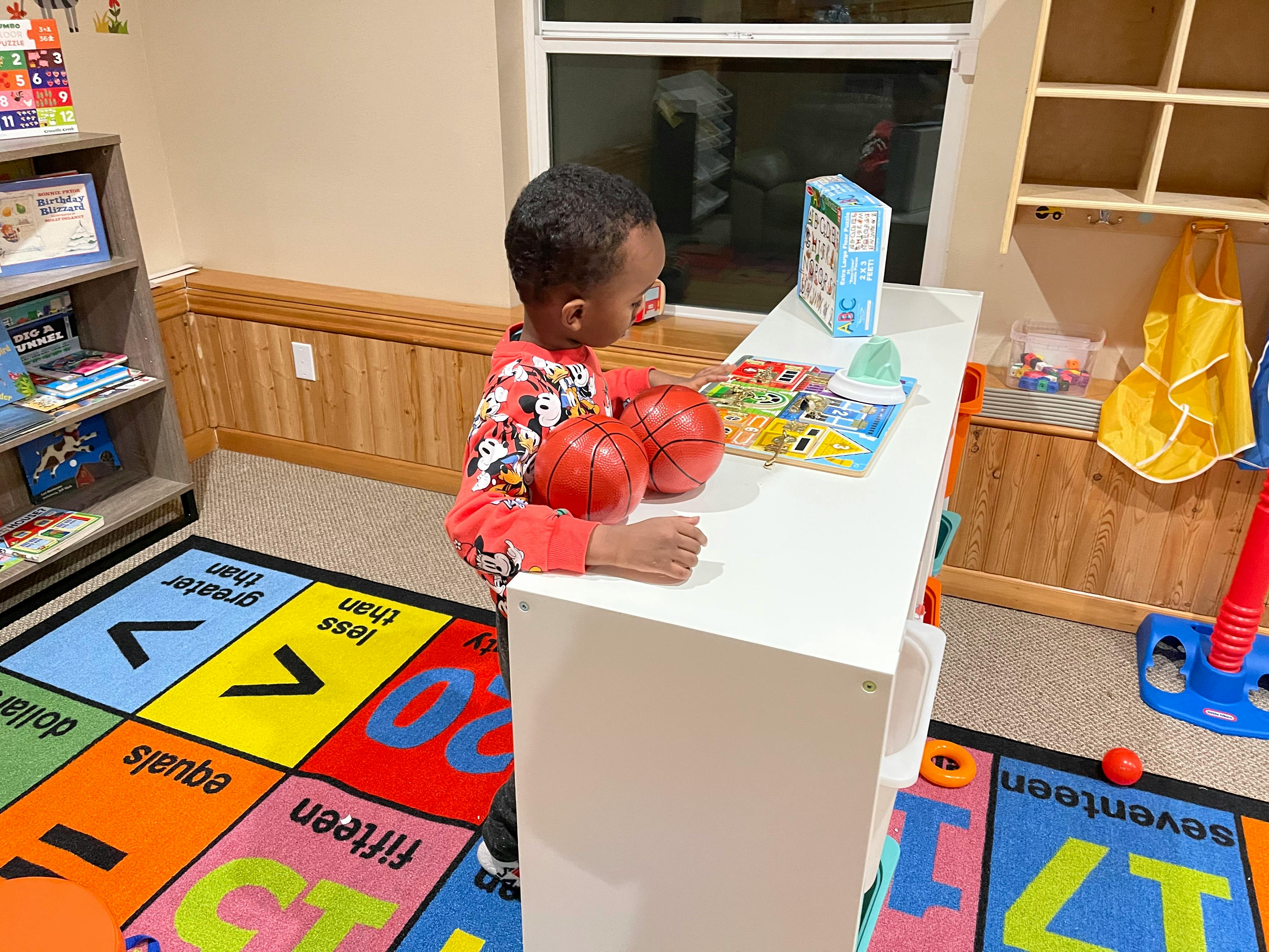 Child standing at a white table with two red balls