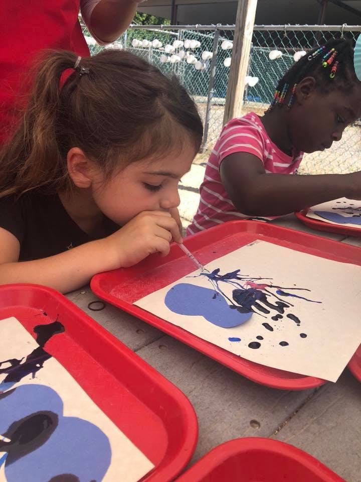 Child blowing paint through a straw onto paper