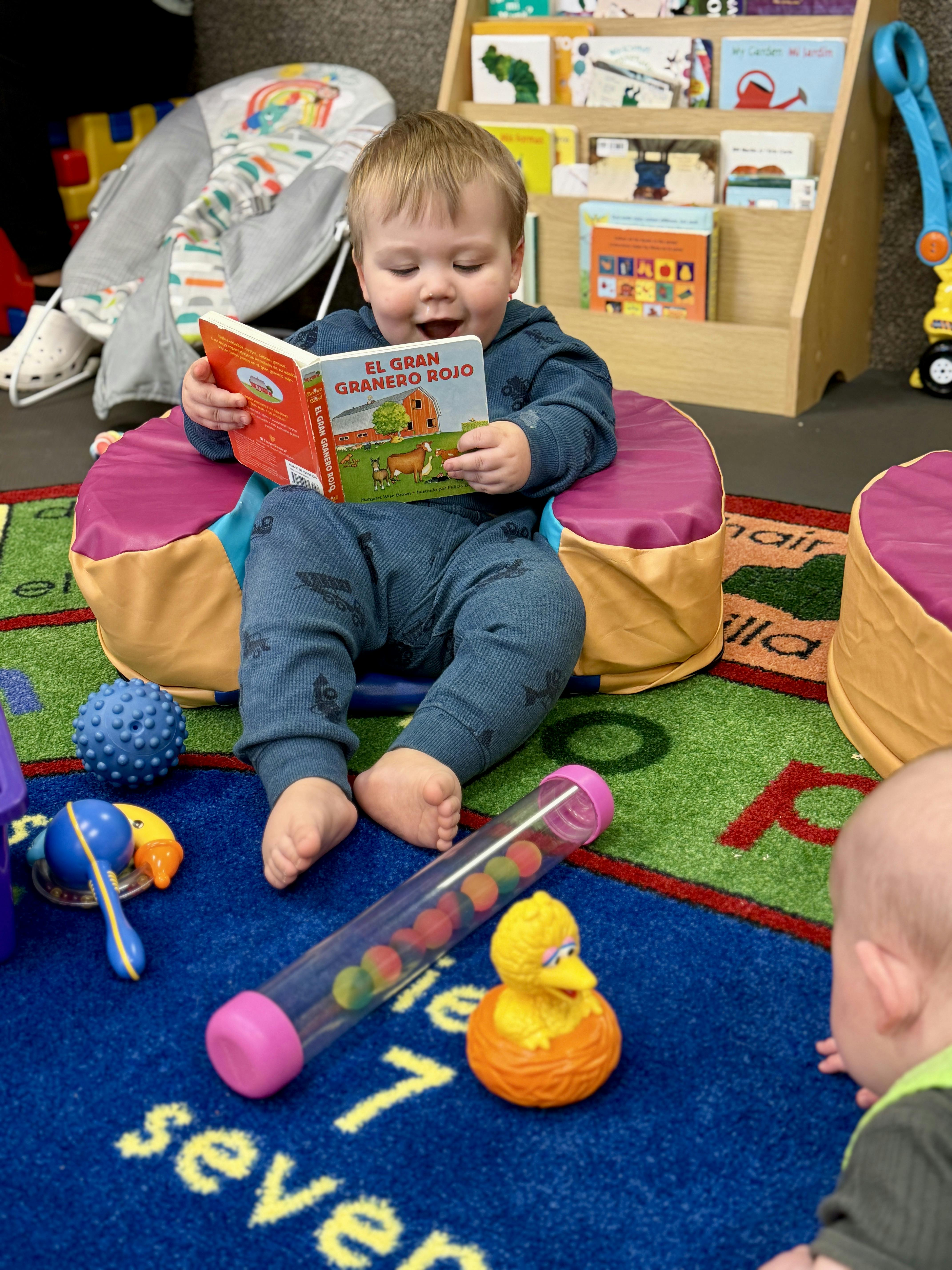 Child sitting on a cushioned seat, reading a book titled "EL GRAN GRANERO ROJO"