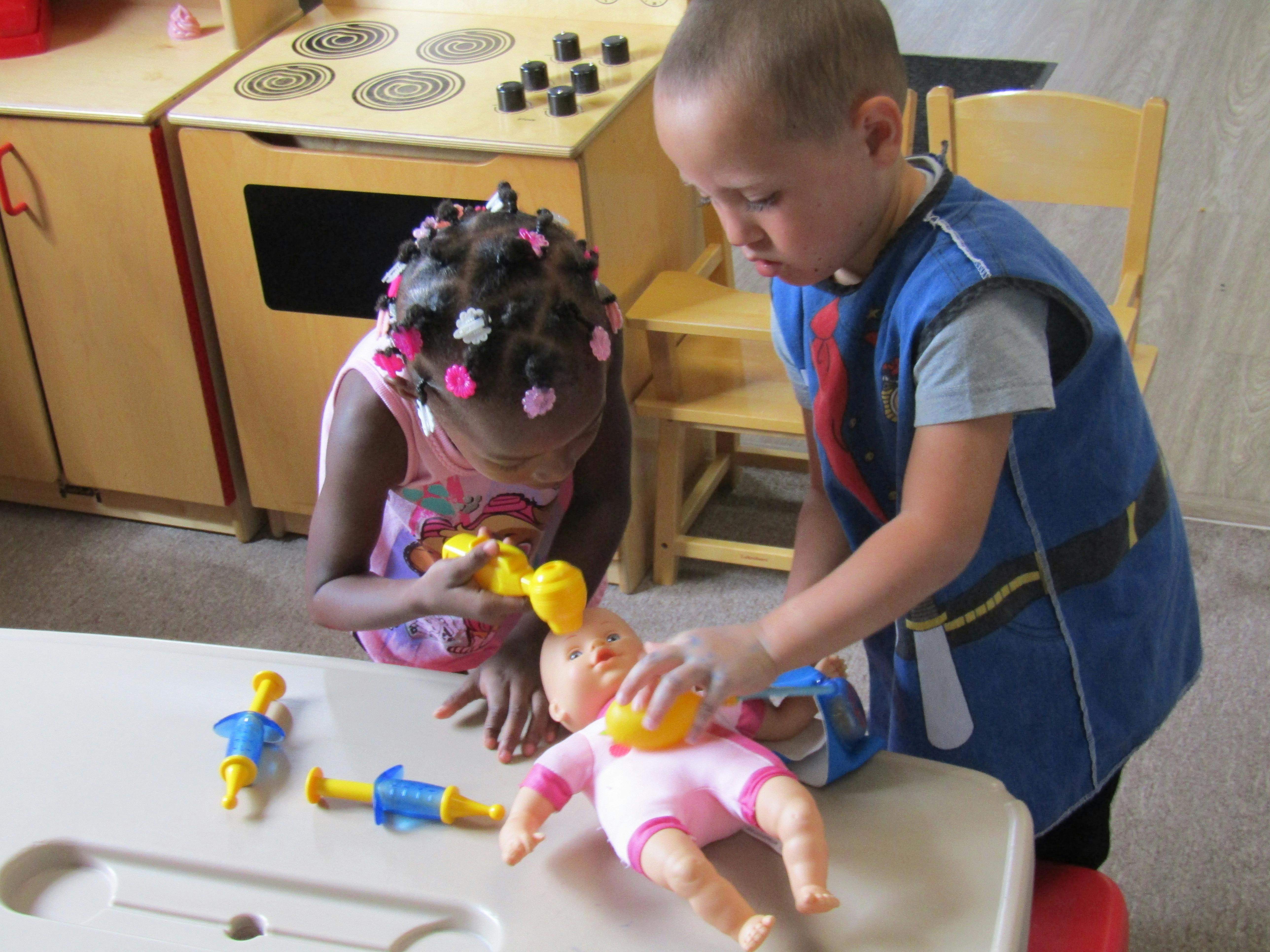 Two children playing with a baby doll and toy medical instruments