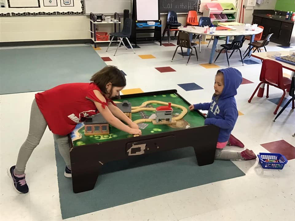 Two children playing with a train set in a classroom