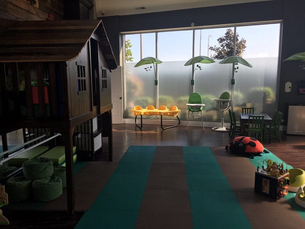Indoor play area with a wooden playhouse, swings, and tables