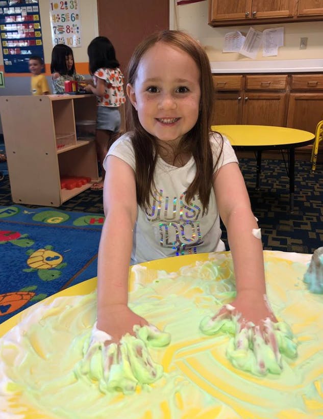Child with hands in green foam on a yellow surface