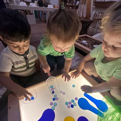 Three children playing with colorful translucent discs on a light table