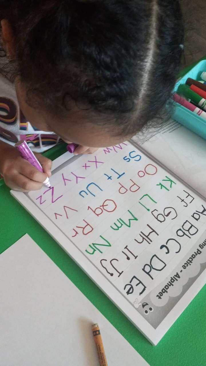 Child writing letters on an alphabet practice sheet