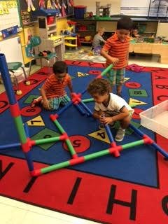 Three children building with colorful plastic tubes in a classroom