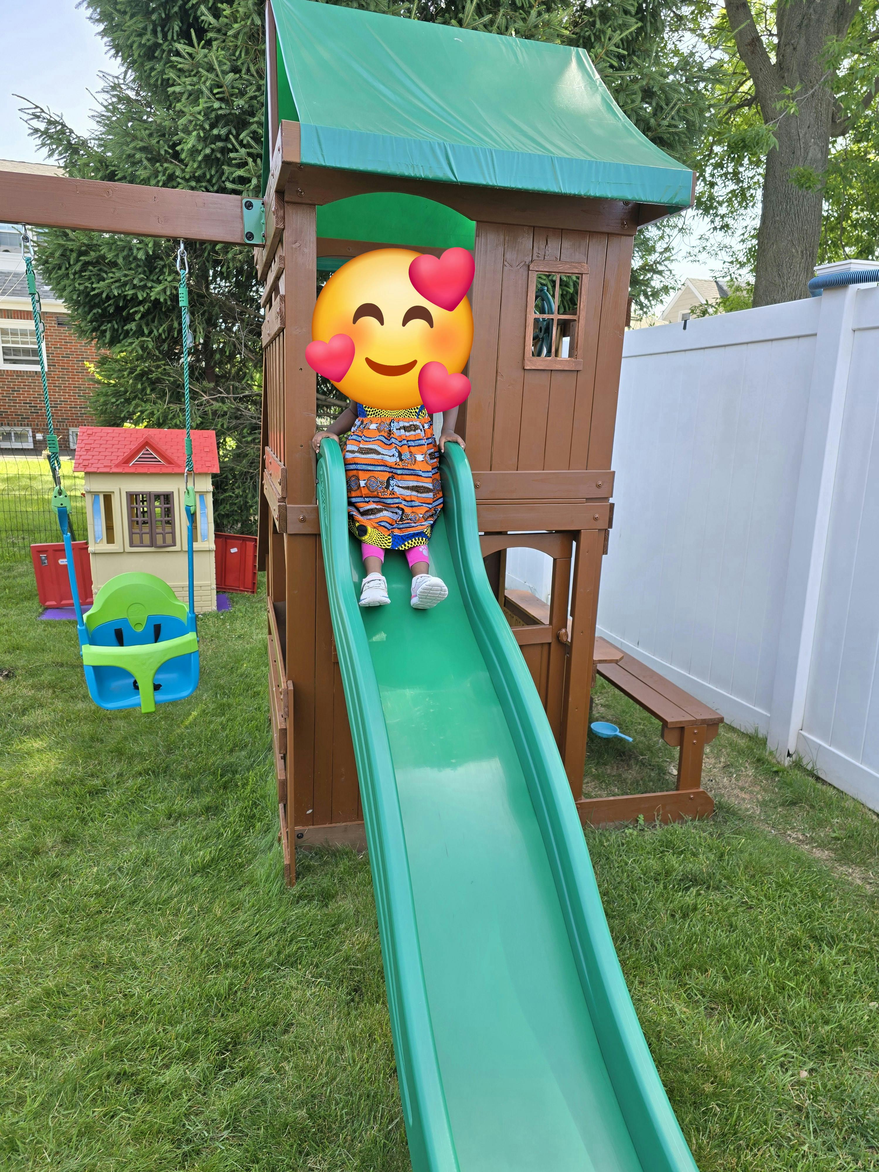 Child on a green slide on a wooden playset