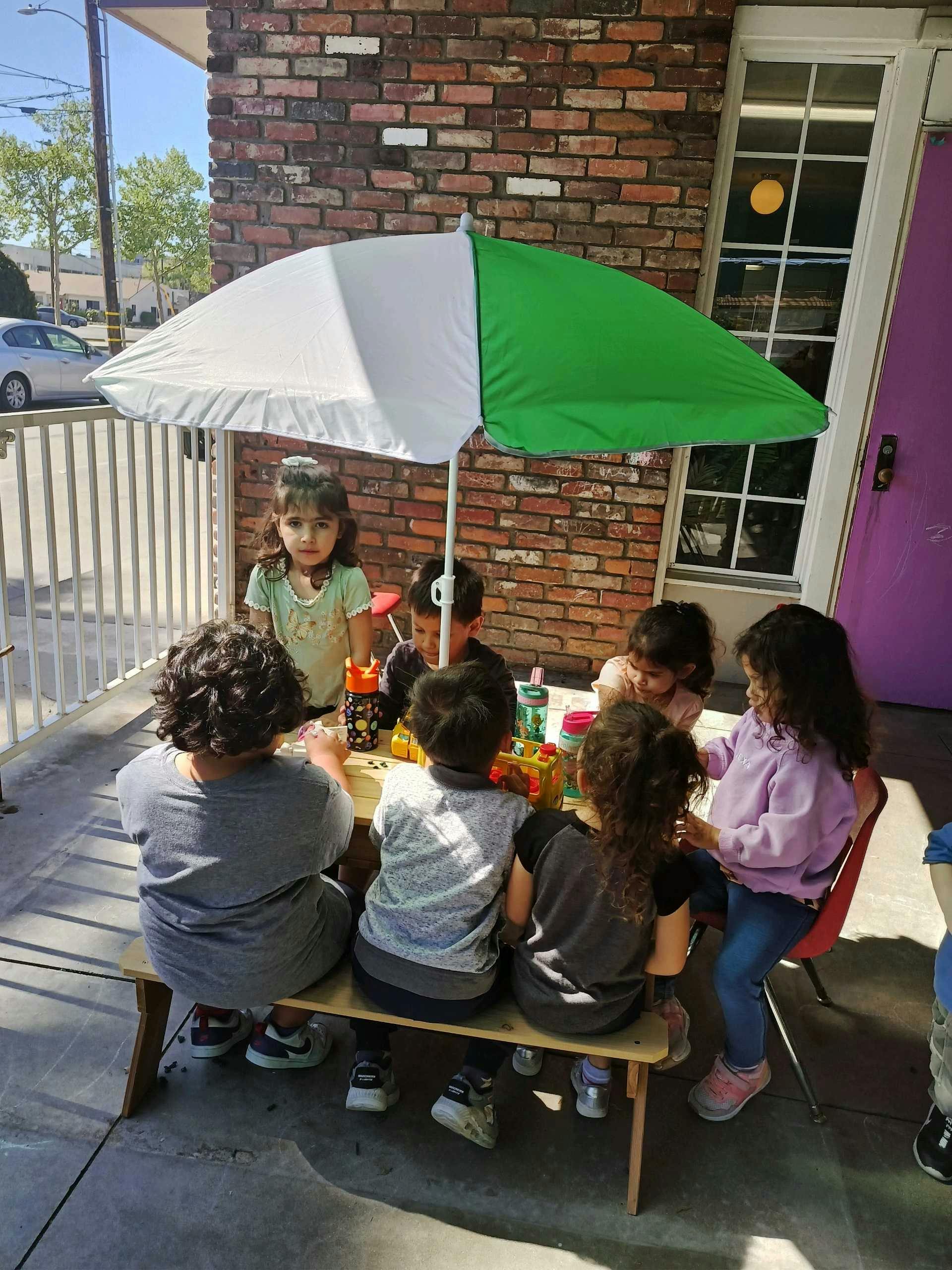 Children sitting at a table under an umbrella