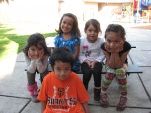 Four children sitting on a bench and one child sitting on the ground