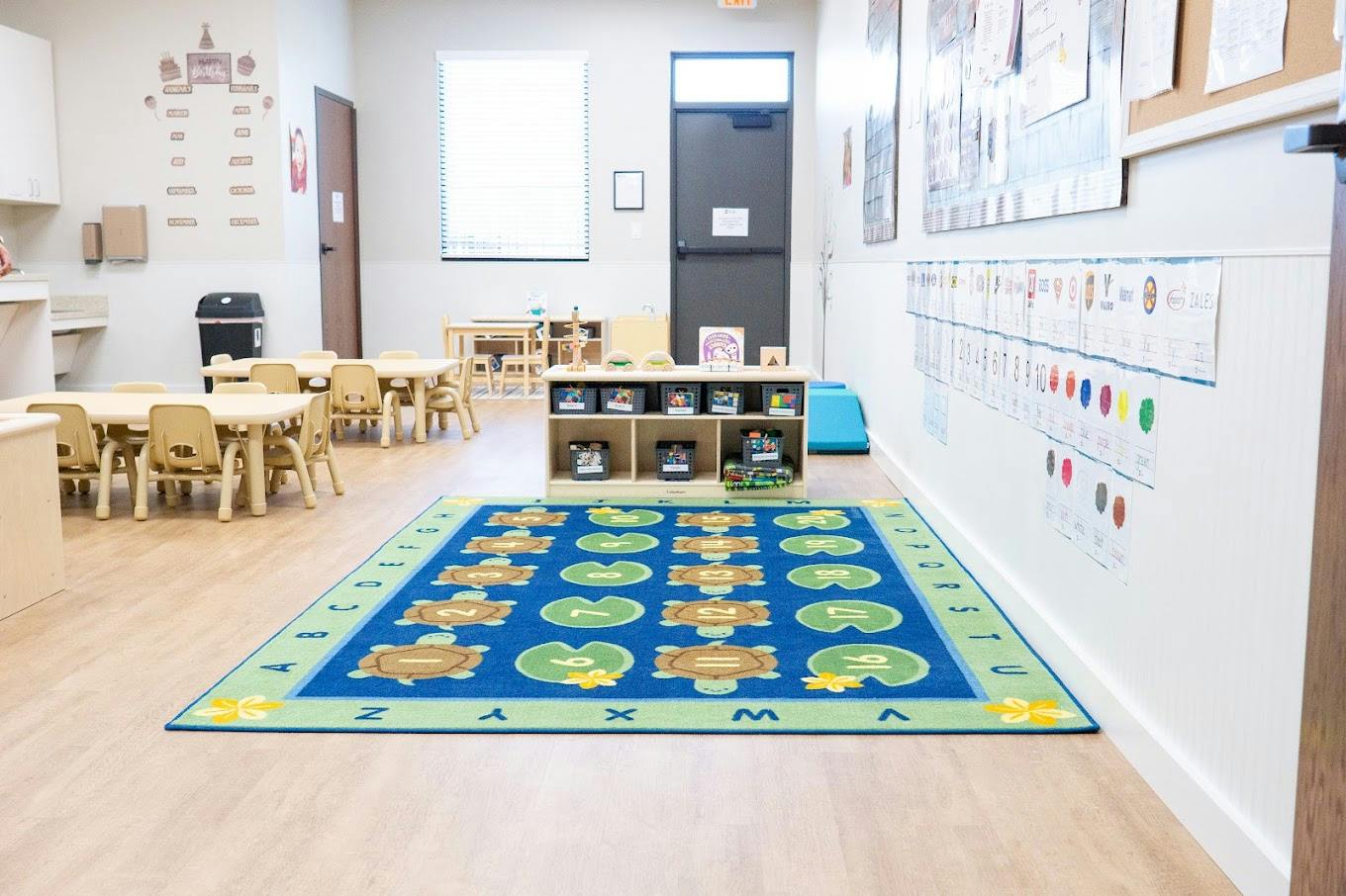 Classroom with small tables and chairs and a colorful rug with numbers