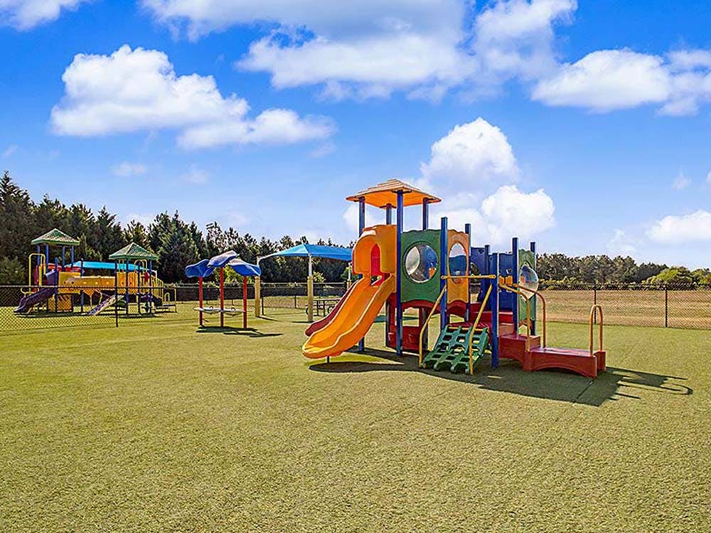 Colorful playground with slides, climbing structures, and shade canopies on grass