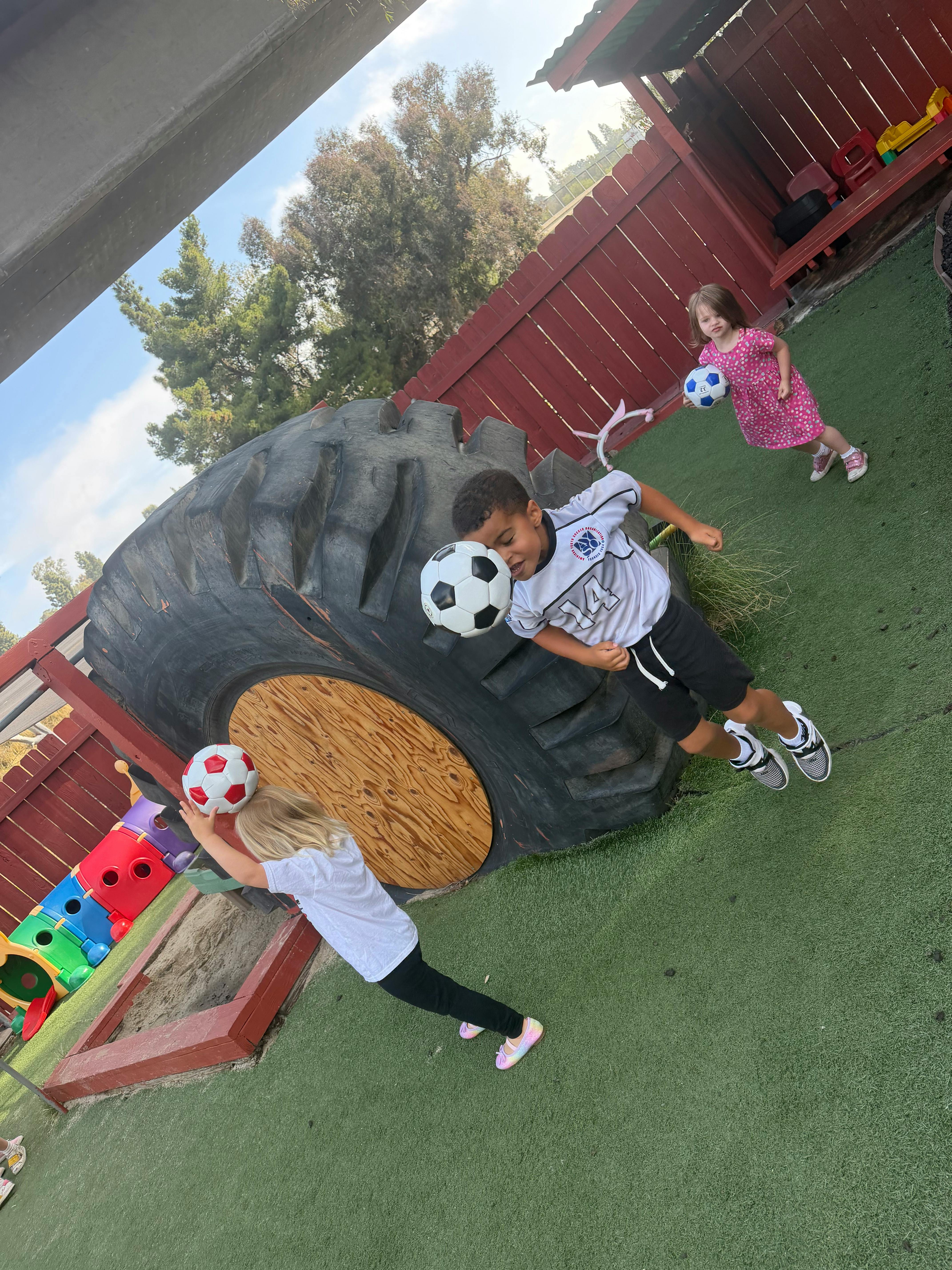 Three children playing with soccer balls on a playground