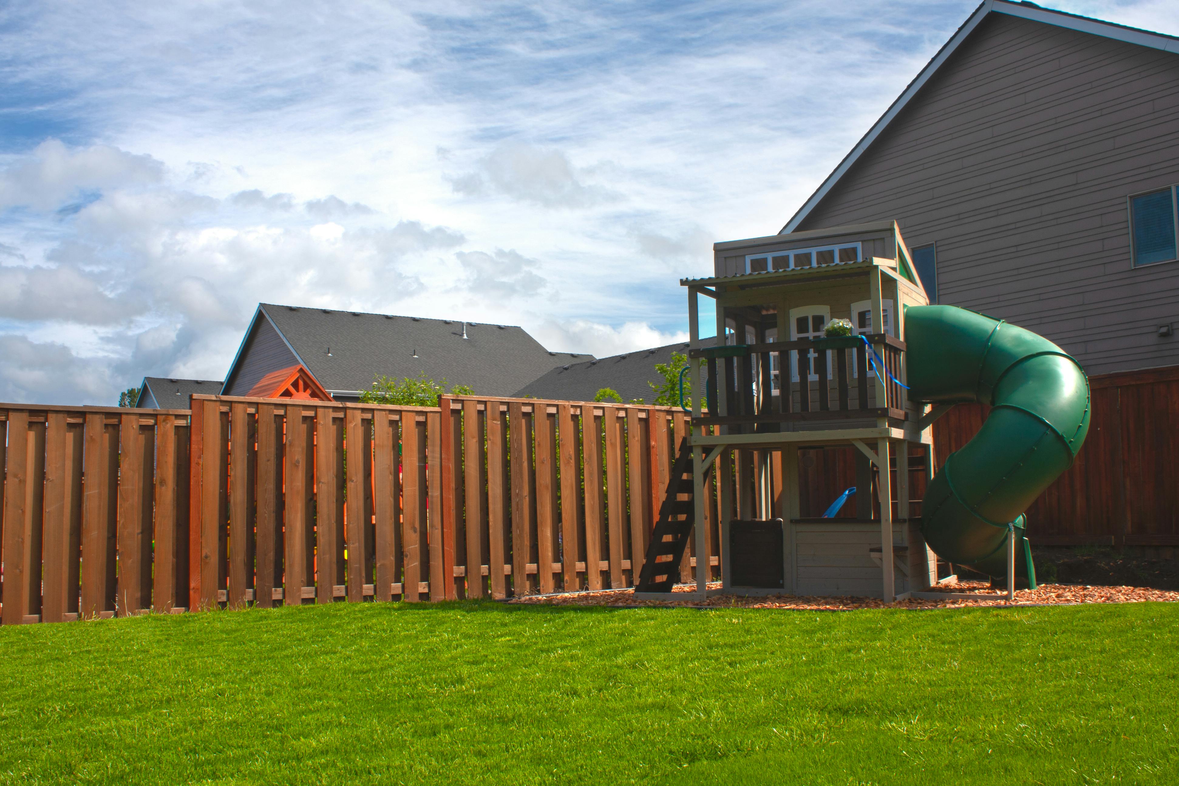 Backyard with a wooden fence, green grass, and a playset with a slide