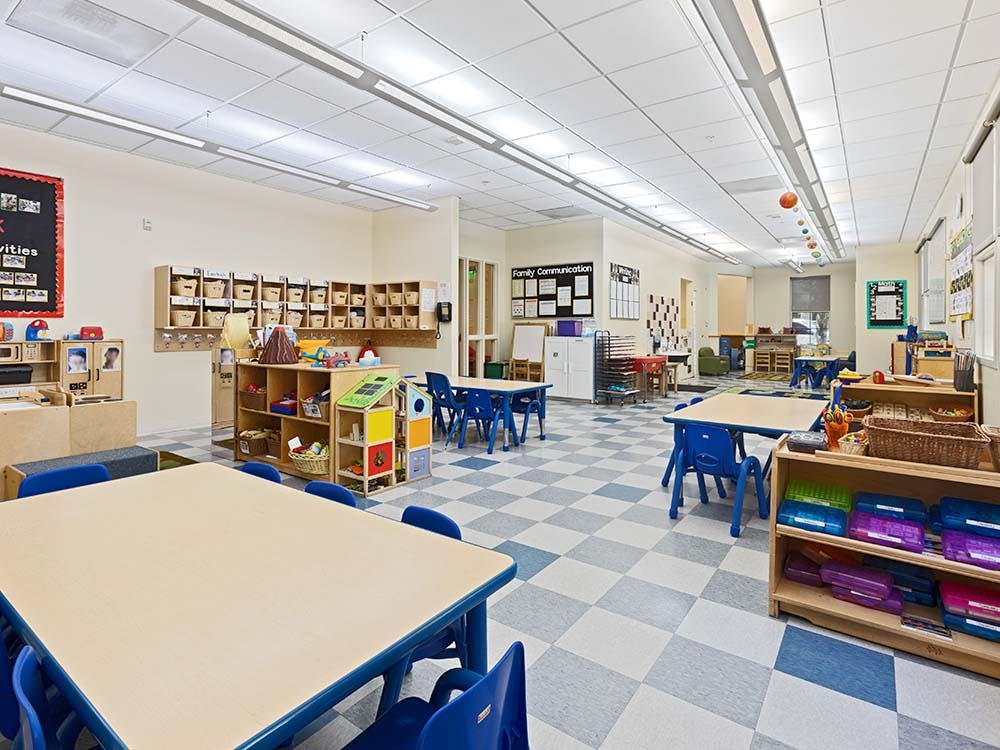 Empty classroom with small tables and chairs, shelves with toys and baskets