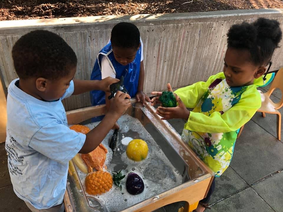 Three children playing with toys in a water table
