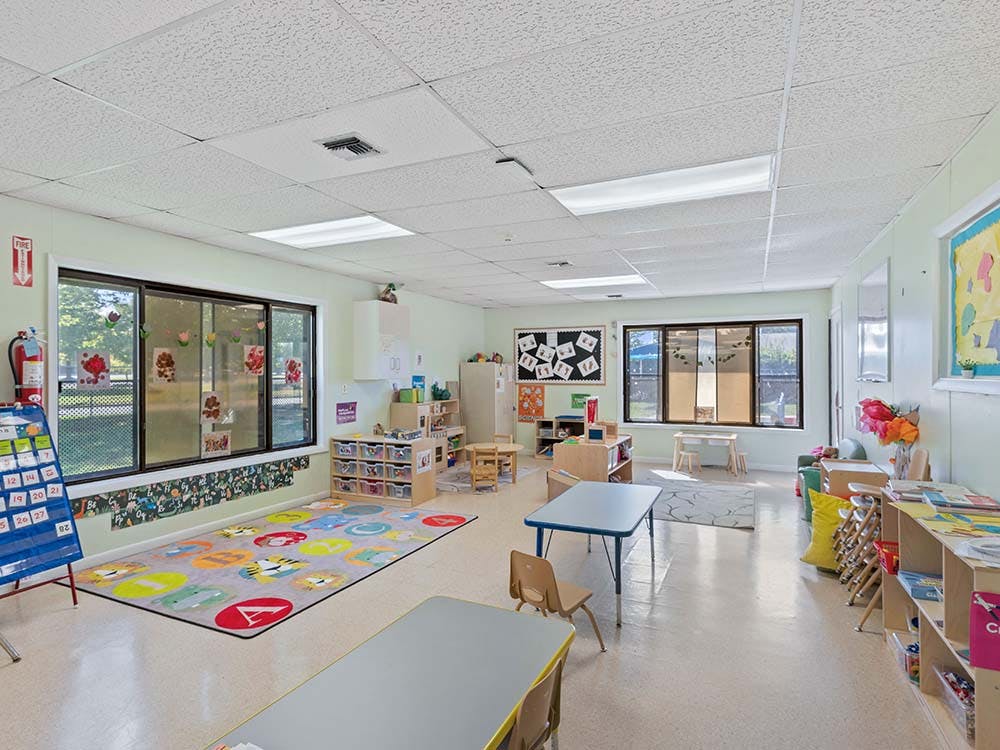 Classroom with child-sized tables and chairs, a colorful rug, and large windows