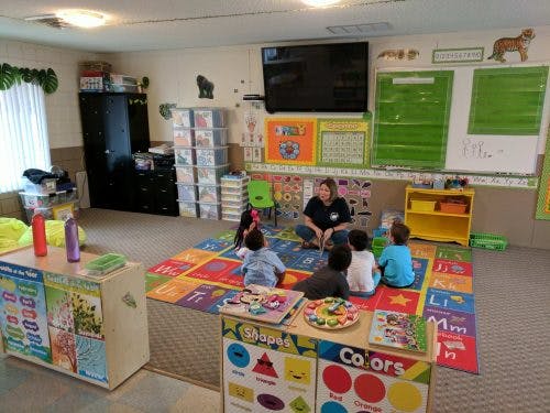 Adult and children sitting on a colorful rug in a classroom