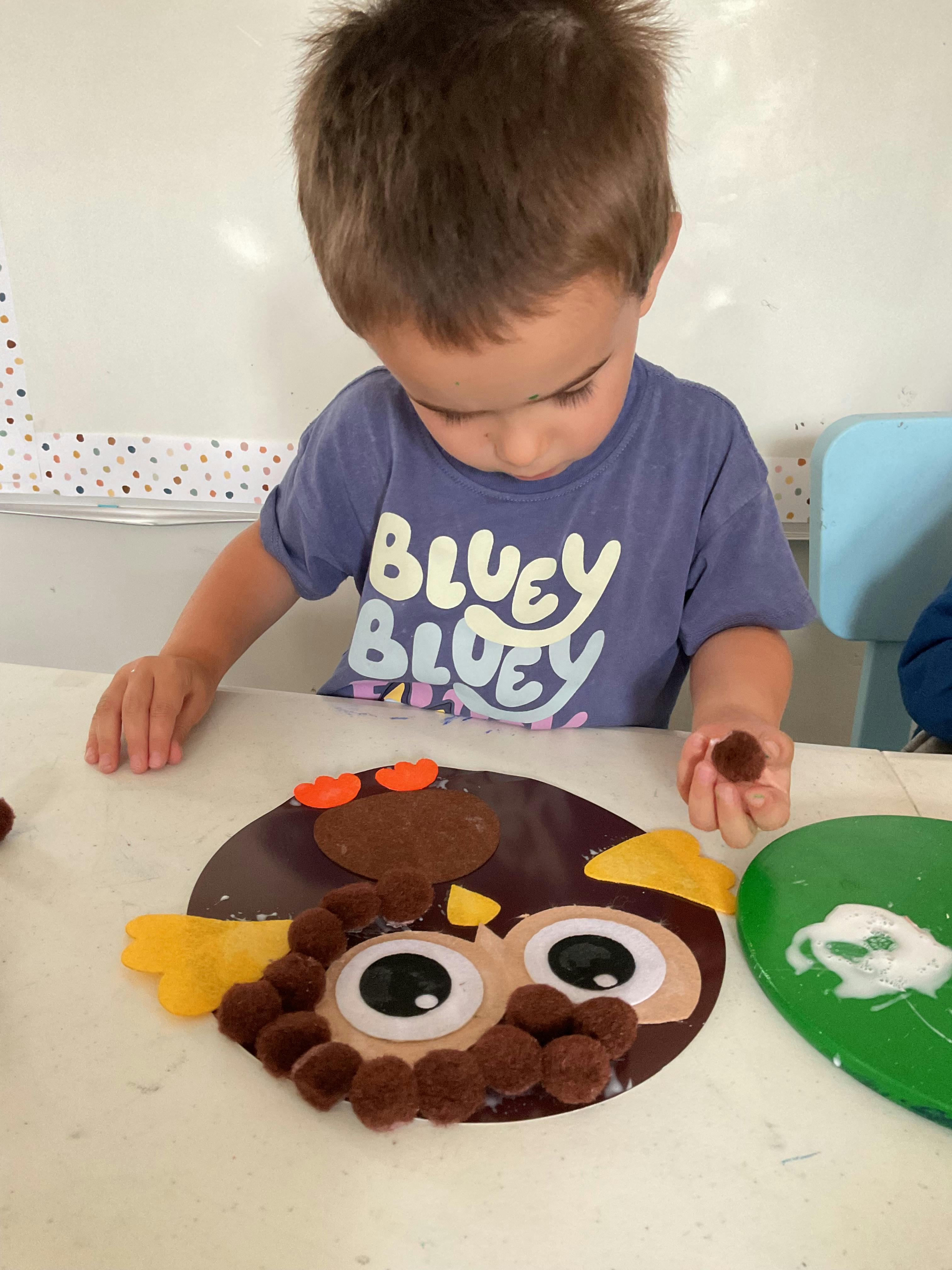 Child crafting an owl out of construction paper and pom-poms