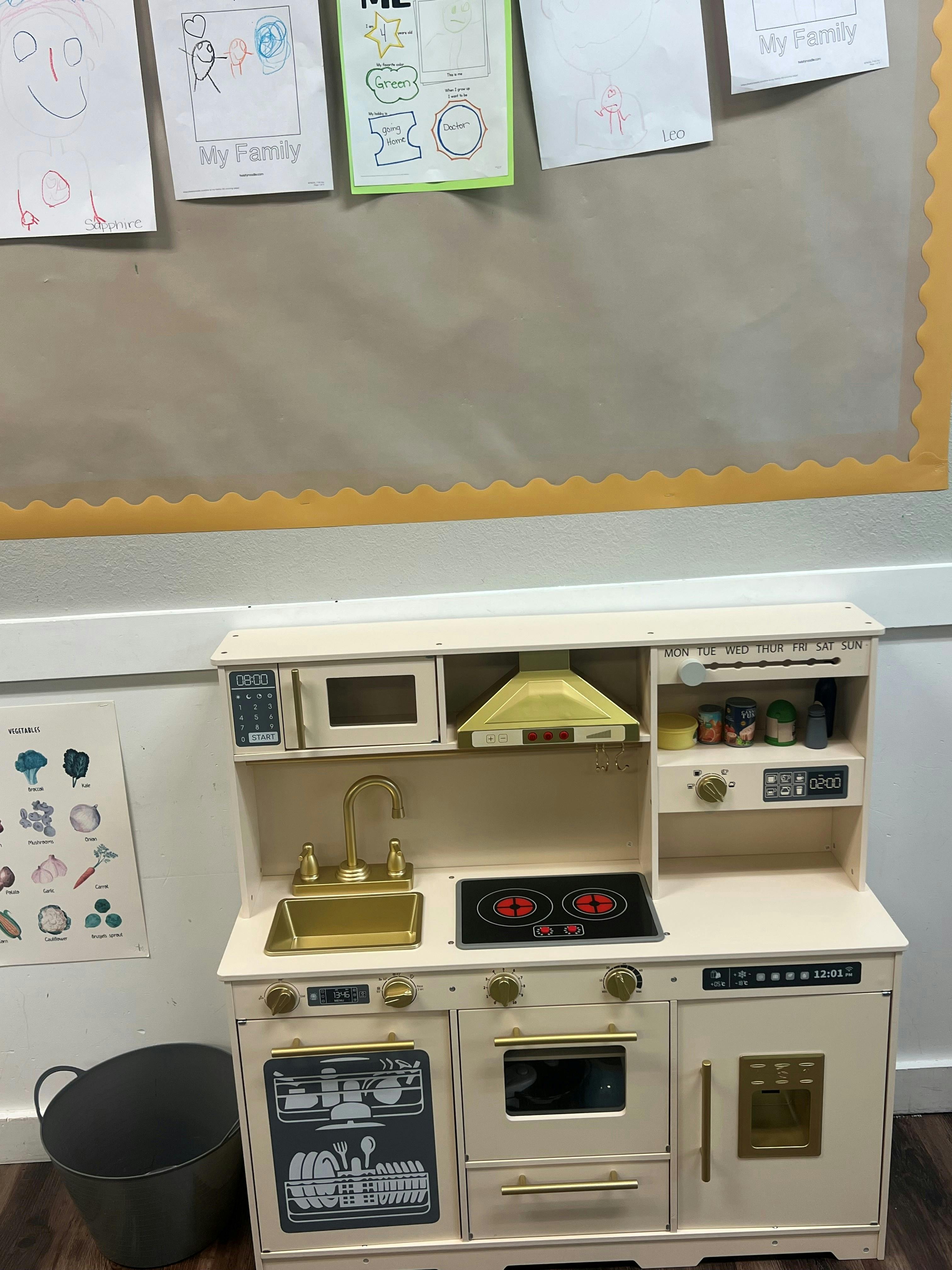Toy kitchen set in a classroom with children's artwork displayed on the wall