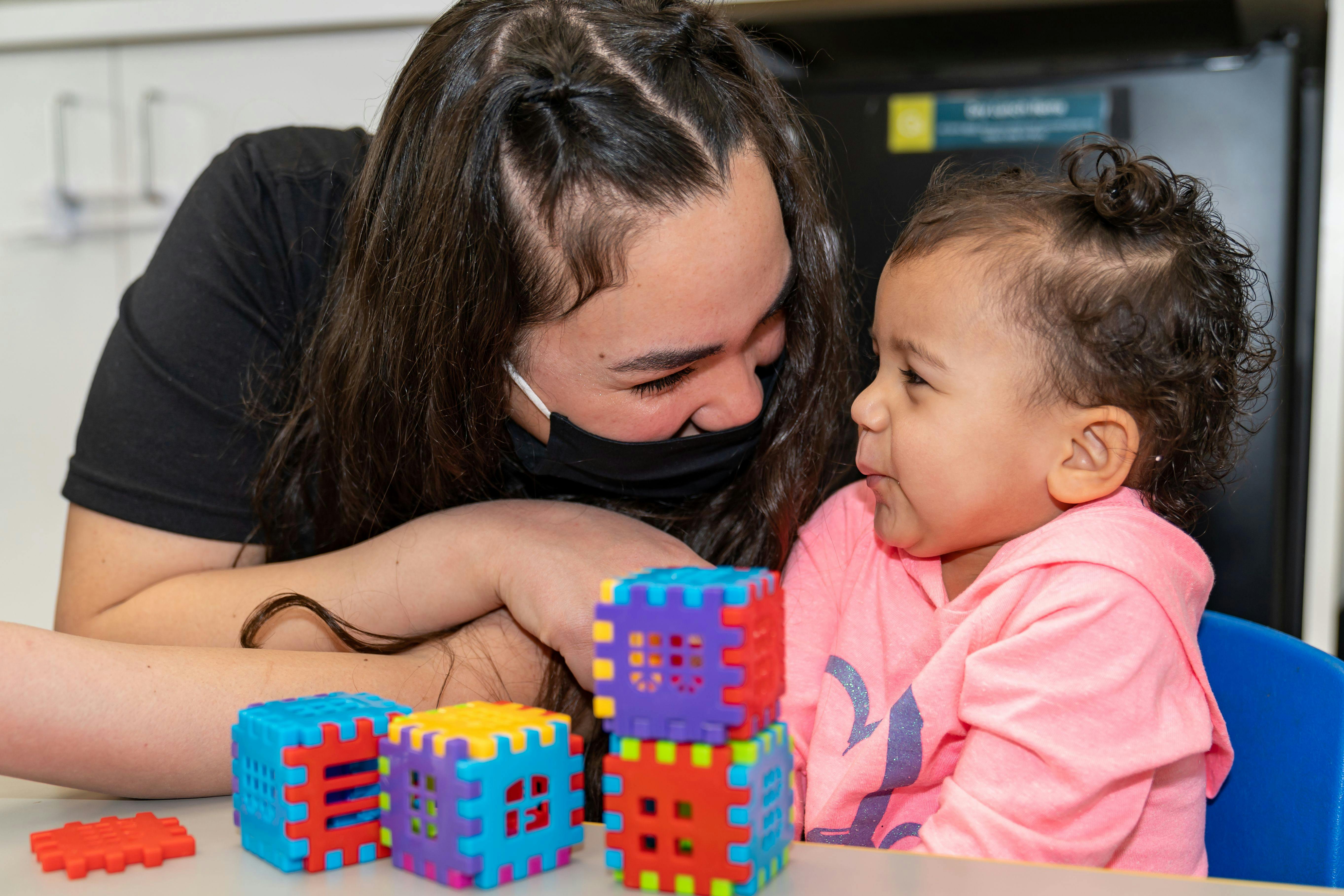 Person in mask looking at child playing with colorful blocks