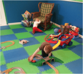 Child playing with a toy train set on a blue and green floor