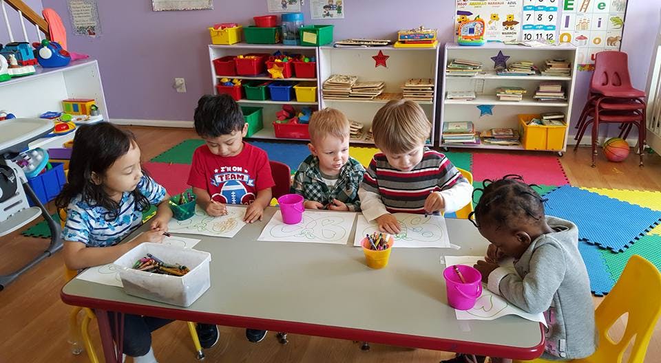 Five children drawing at a table in a classroom