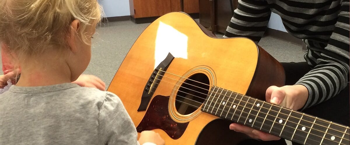 Child looking at a person holding an acoustic guitar