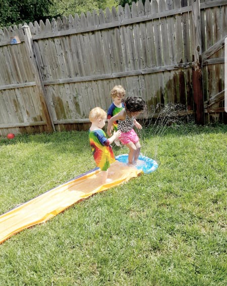 Three children playing with a slip and slide in a grassy yard